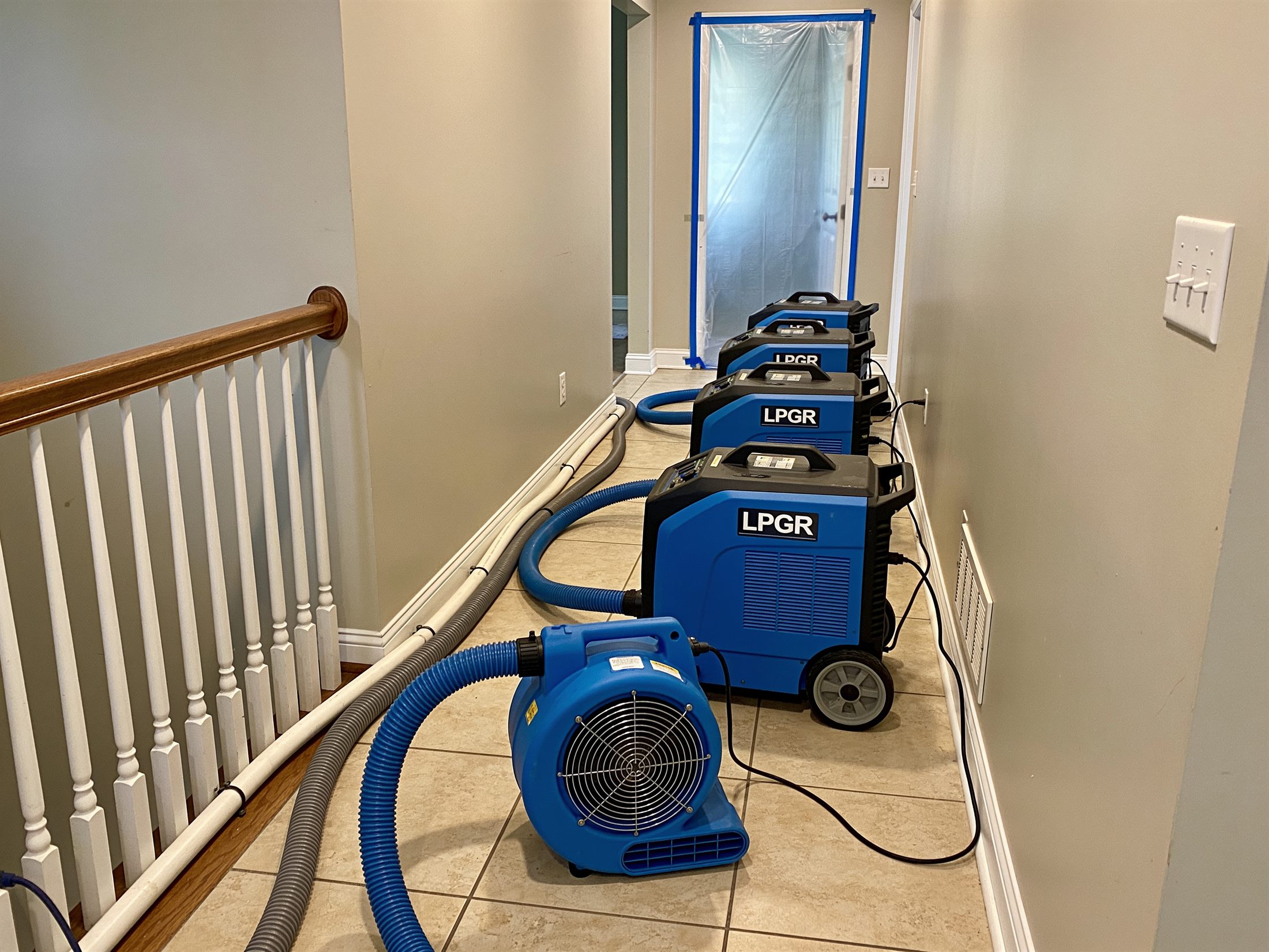 Industrial dehumidifiers and low-profile air movers drying a residential hallway